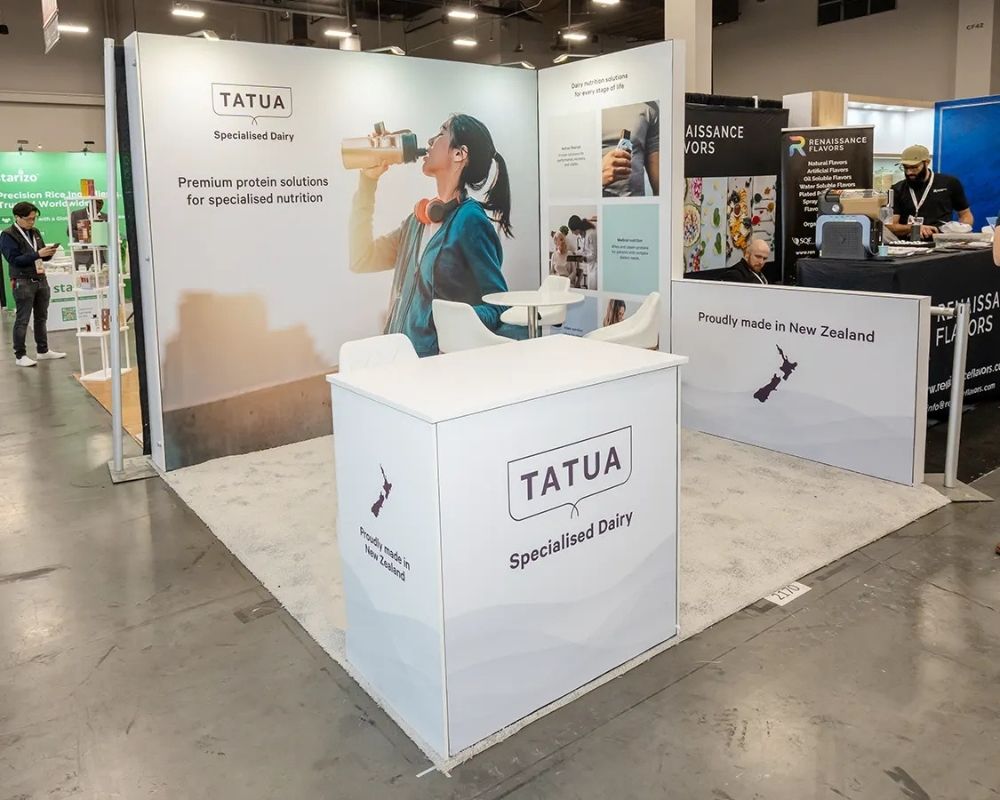 TATUA specialized dairy trade show booth featuring promotional images of dairy nutrition and their premium protein solutions. Display highlights 'Proudly made in New Zealand.'