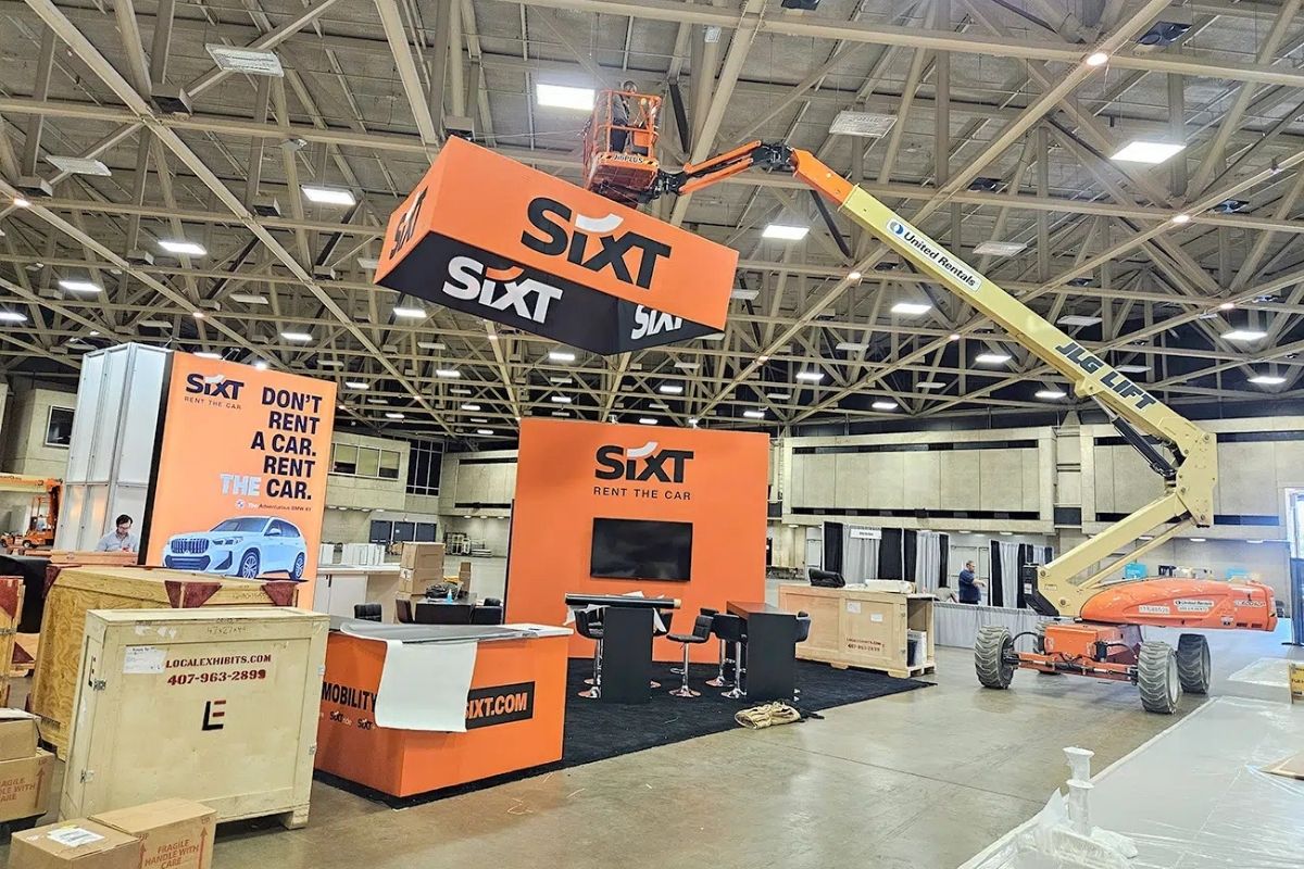 Trade show booth installation with hanging banner structure and lift equipment by Local Exhibits