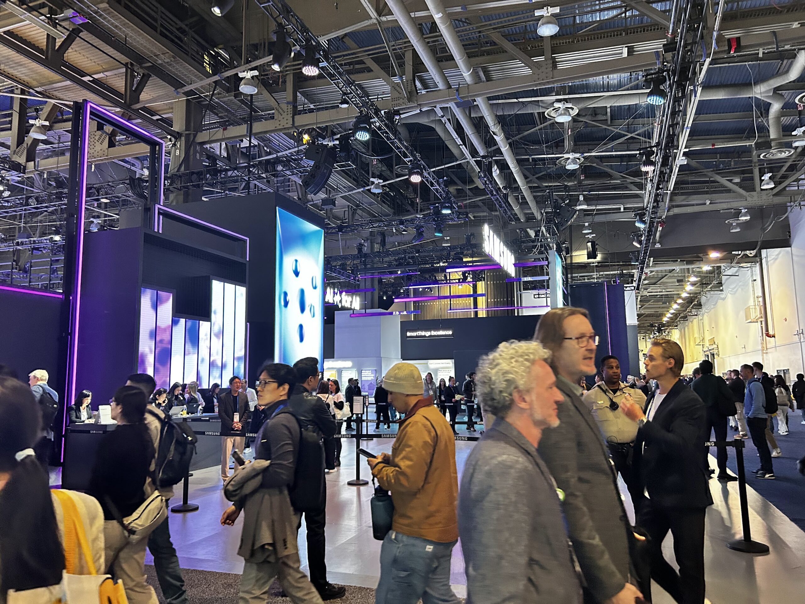 CES exhibit hall with Samsung technology displays, modern booth lighting, and attendees walking through the show floor