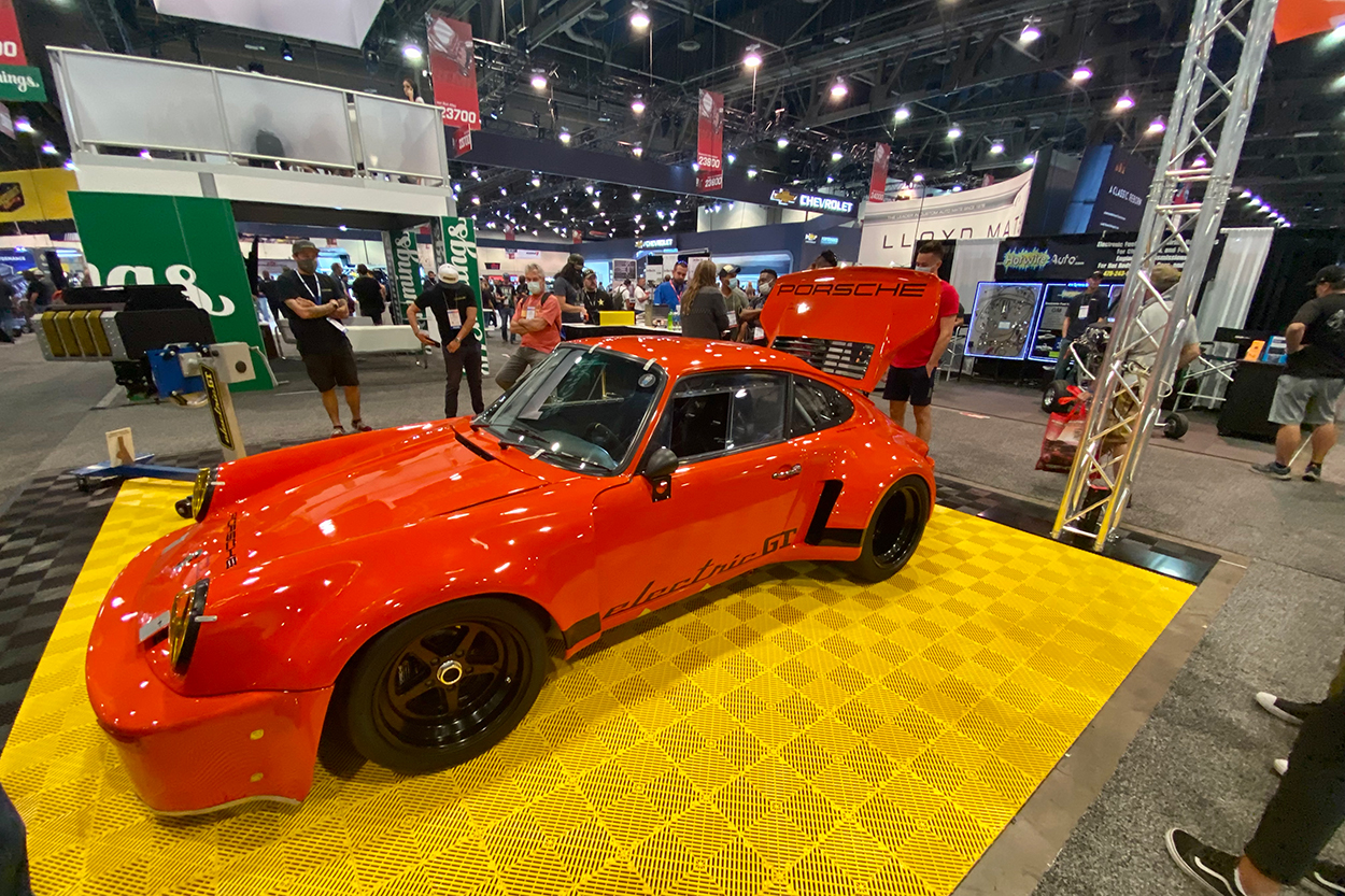 SEMA Show exhibit booth with bright orange Porsche display, yellow flooring, and attendees viewing custom automotive builds