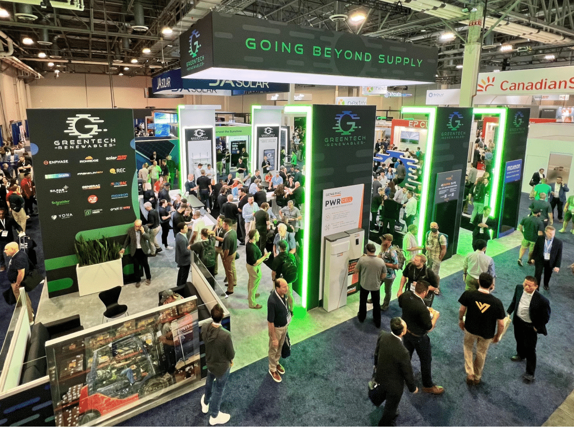 Aerial view of the Greentech Renewables booth at a trade show with vibrant green lighting, product displays, and attendees interacting with exhibitors.