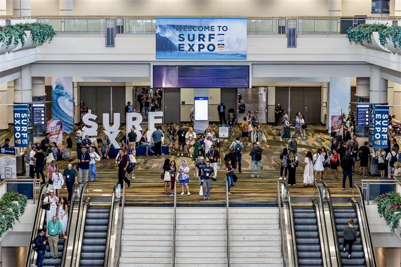 Entrance to Surf Expo with large signage, escalators, and attendees entering the event venue.